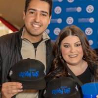 Two alums holding up their Red Wings and Lakers co-branded hats.